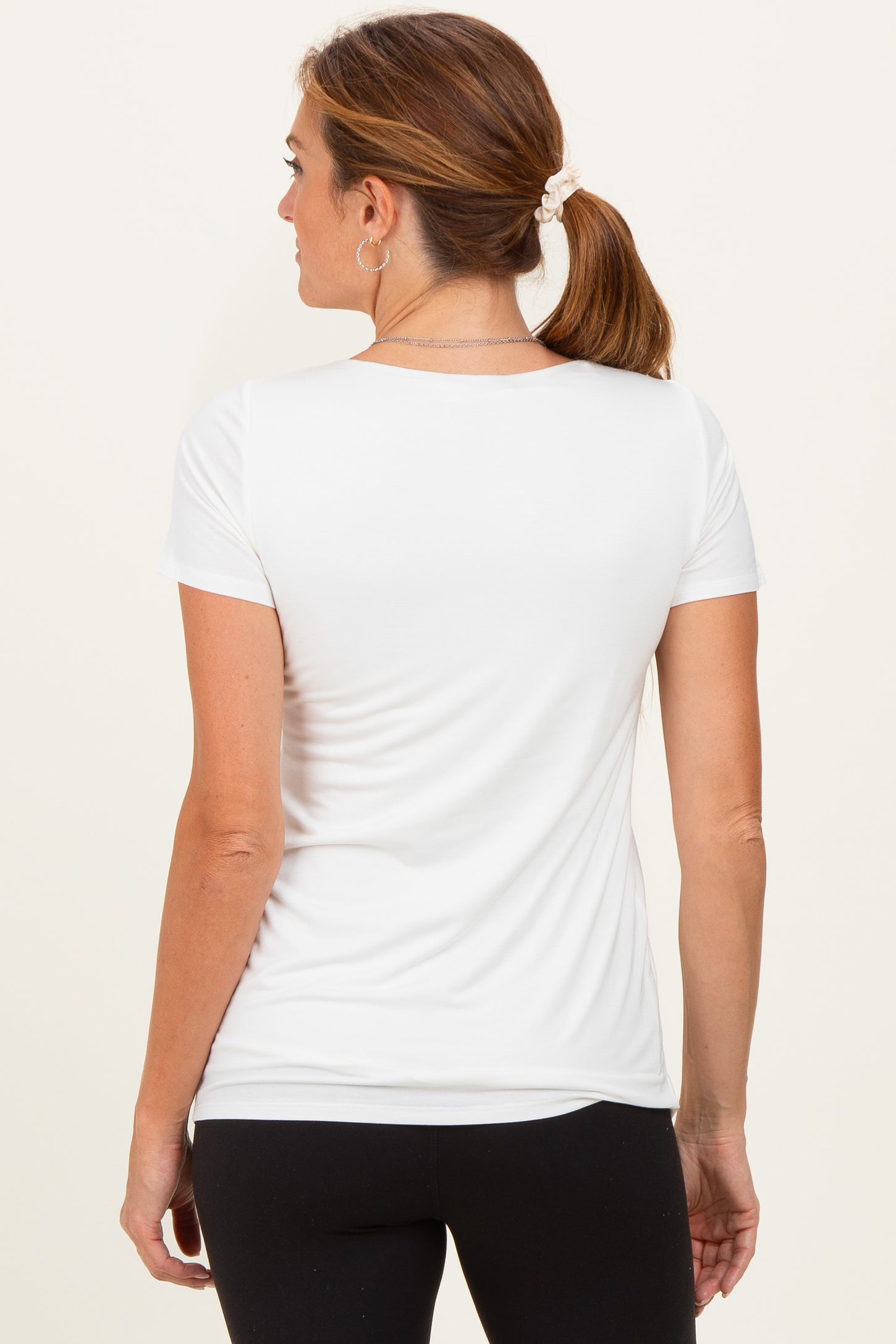 woman wearing a white short sleeve top, seen from the back, paired with black leggings