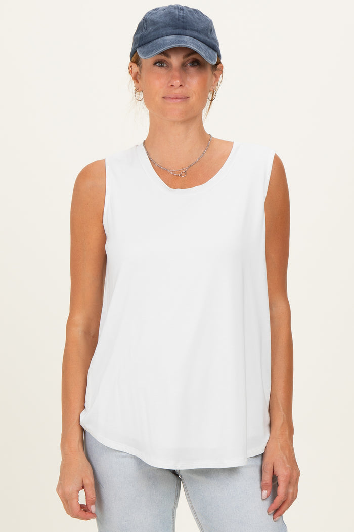 woman wearing a white sleeveless top with a v-neck and light blue jeans, paired with a navy baseball cap