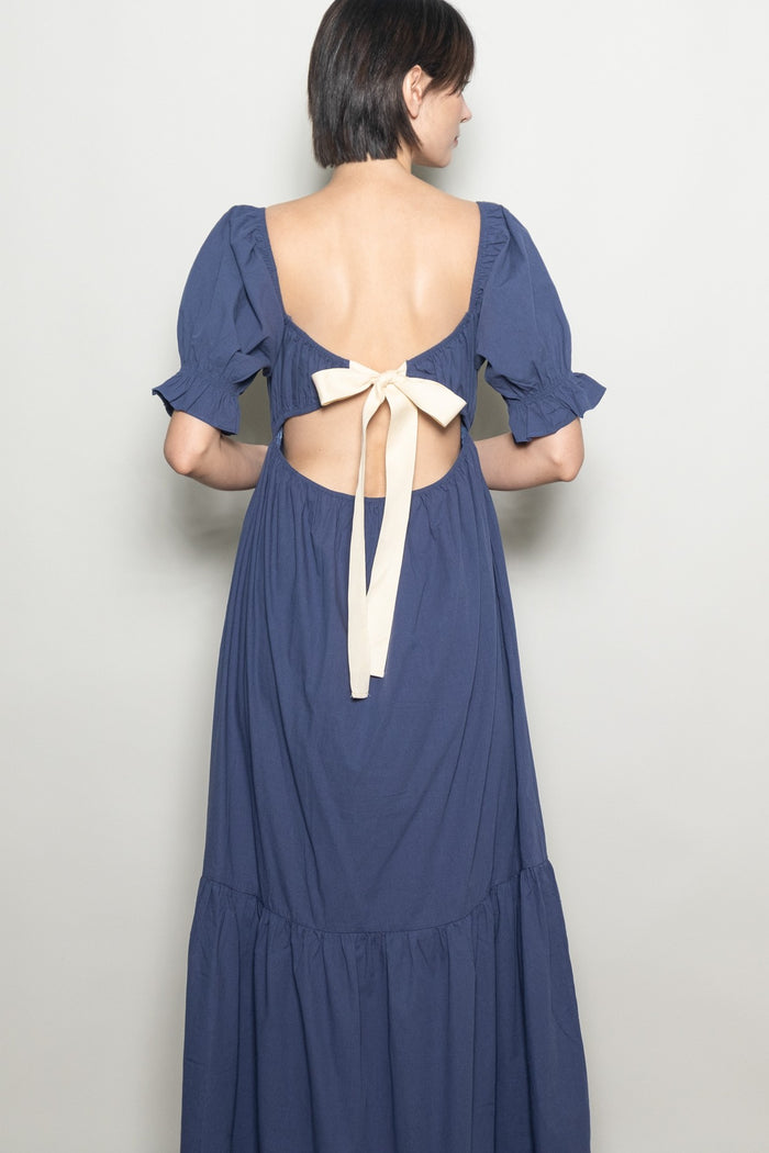 woman wearing a navy blue dress with puff sleeves and an open back featuring a tied bow detail