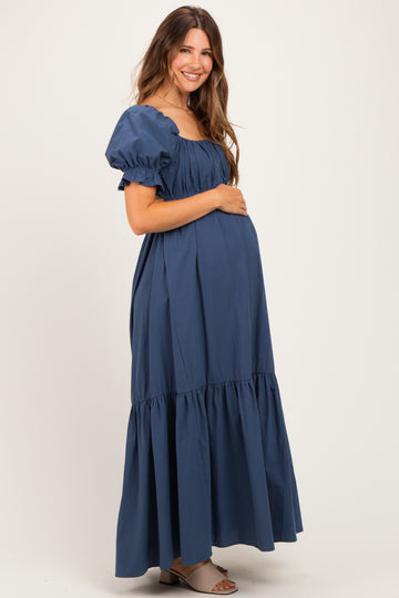 woman wearing a navy blue maternity maxi dress with puff sleeves and a tiered skirt, showcasing her baby bump