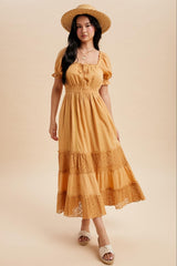 woman wearing a mustard yellow tiered midi dress with lace detailing and puff sleeves, accessorized with a straw hat