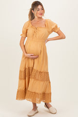woman wearing a mustard yellow maternity maxi dress with lace details and holding her baby bump