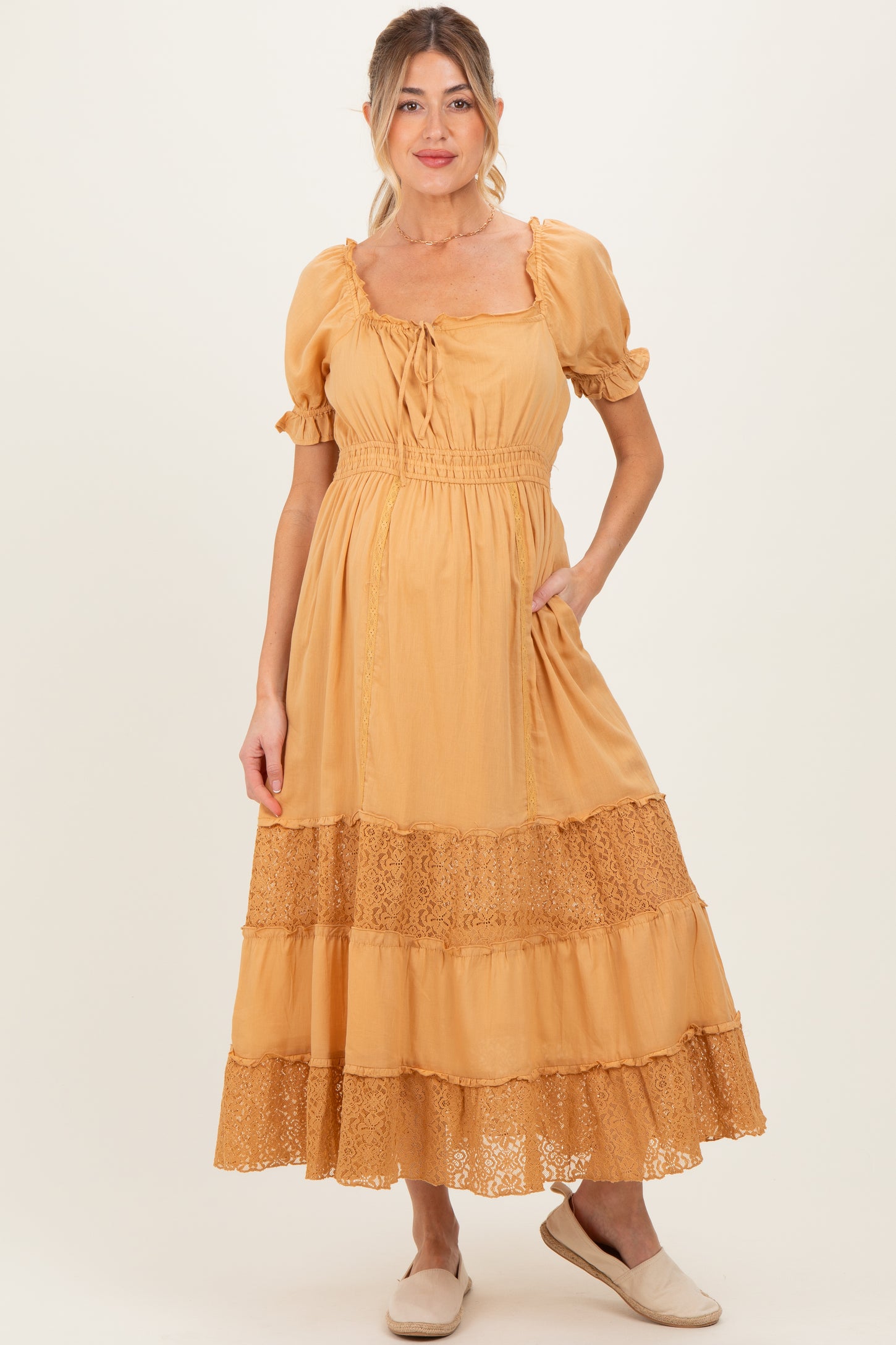 woman wearing a mustard yellow maternity dress with short puff sleeves and lace trim, featuring a tie at the neckline and pockets