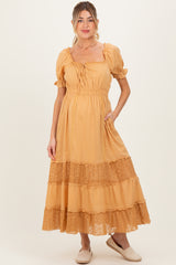 woman wearing a mustard yellow maternity dress with short puff sleeves and lace trim, featuring a tie at the neckline and pockets