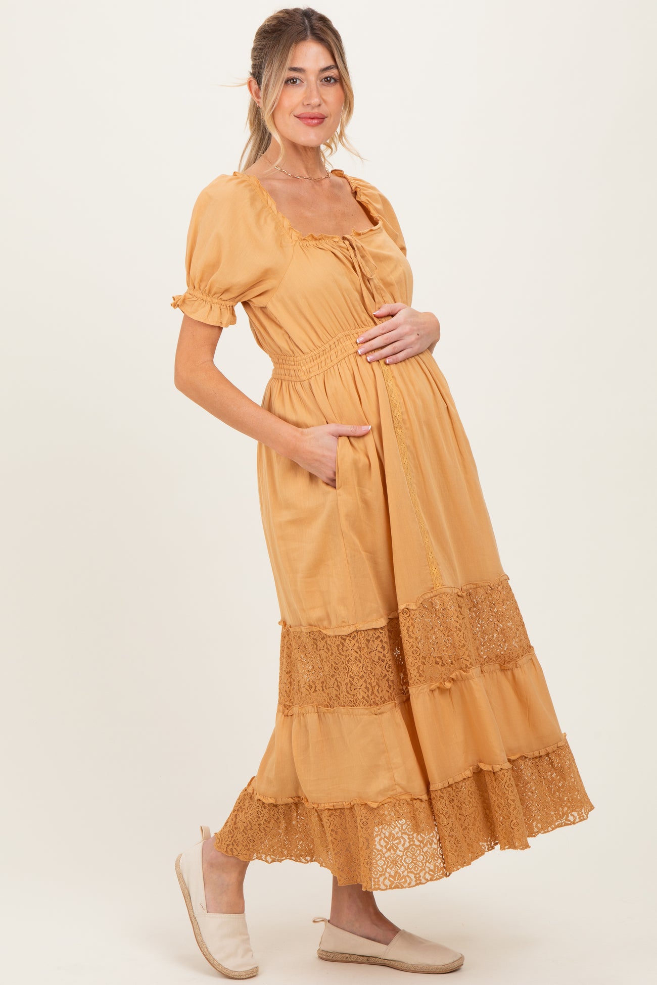 woman wearing a mustard yellow maternity maxi dress with pockets and lace trim, holding her baby bump