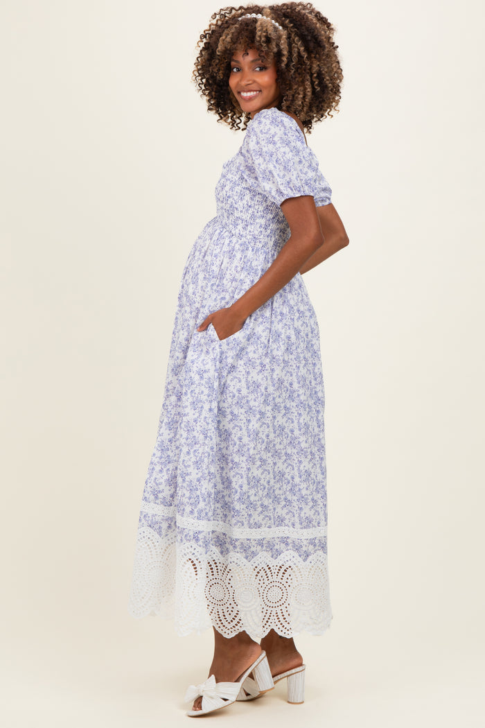 woman wearing a lavender floral maternity dress with puff sleeves and lace hem, showing her baby bump and standing sideways