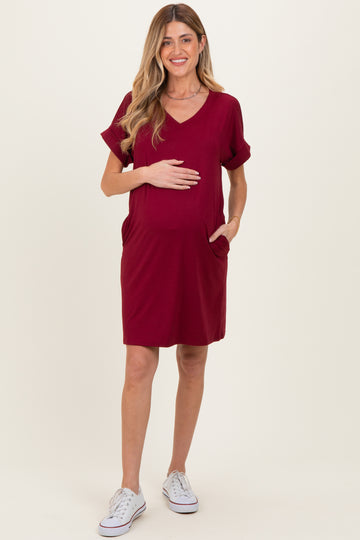 woman wearing a burgundy short sleeve maternity dress with pockets and a visible baby bump