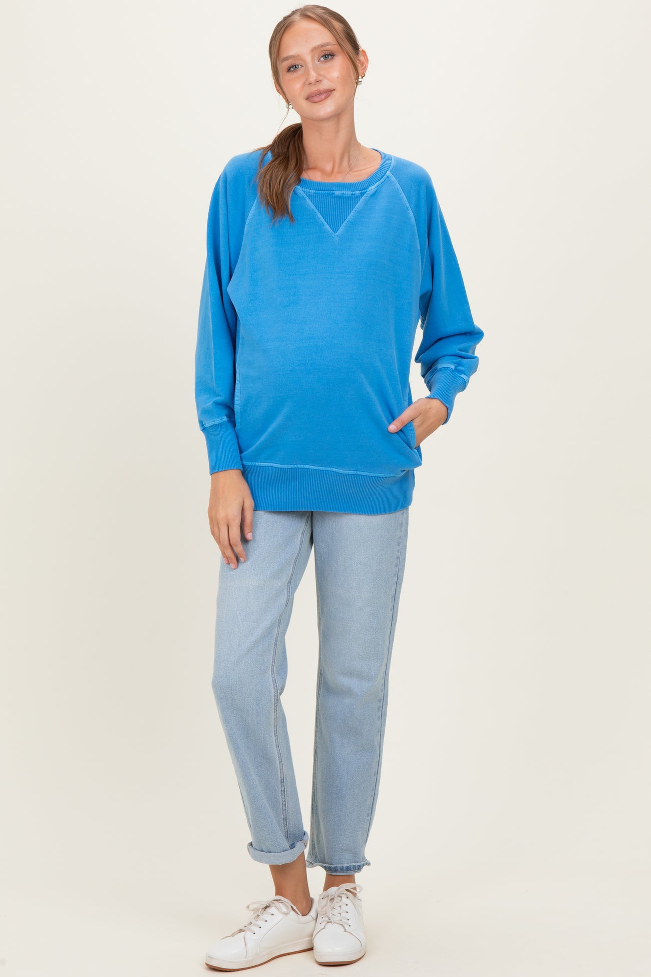 woman wearing a vibrant blue maternity sweatshirt with a relaxed fit and front pocket, paired with light wash jeans and white sneakers