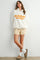 woman wearing a cream fleece pullover with "SUNDAY MORNING" text and striped shorts, styled with socks and slippers