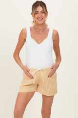 woman wearing a white maternity tank top and yellow striped maternity shorts, holding her baby bump