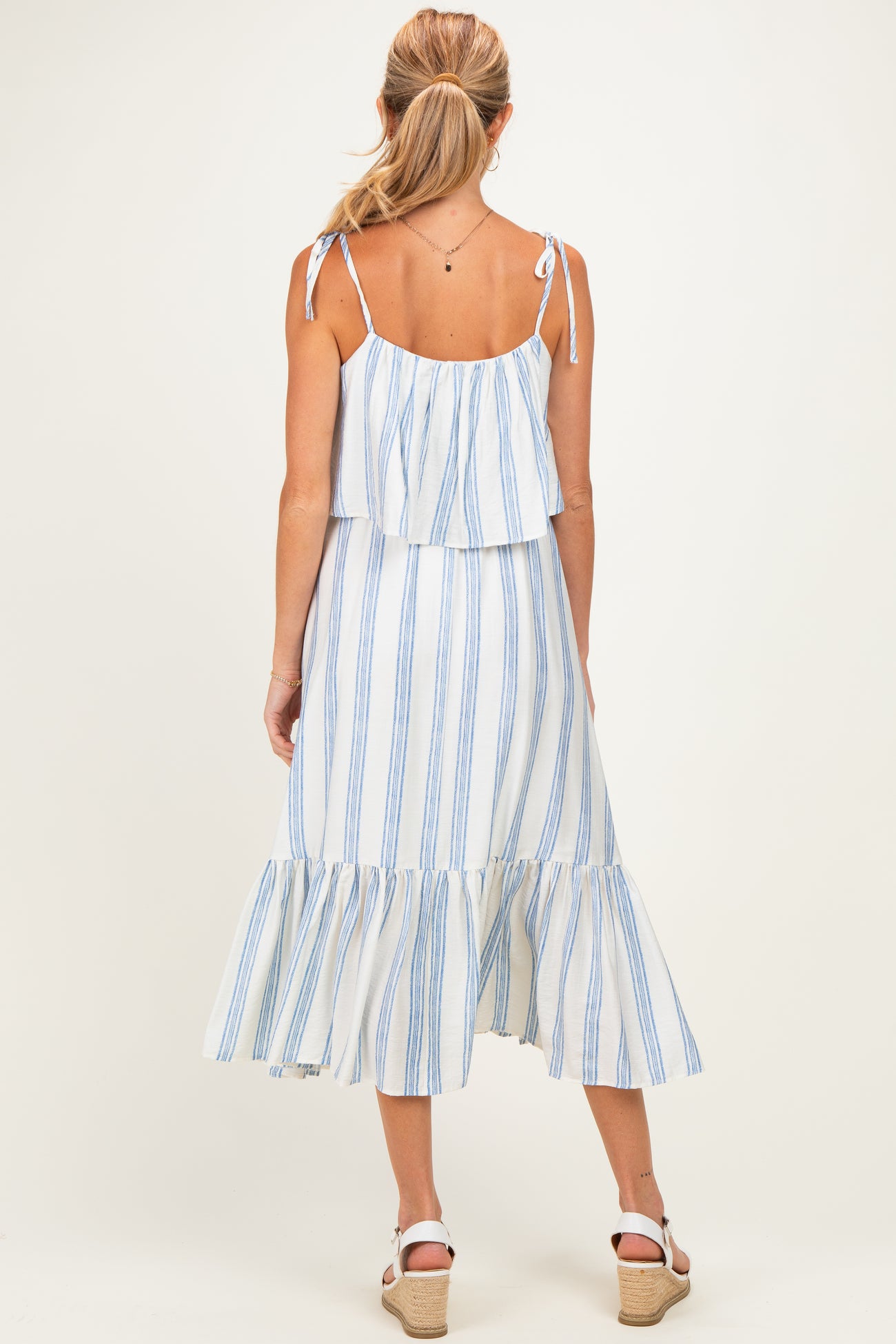 woman wearing a white and blue striped maternity dress with a flowy hem and adjustable straps, showing her back