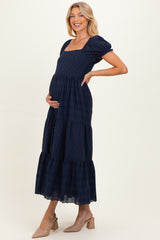 woman wearing a navy blue maternity maxi dress with puff sleeves and a tiered skirt, cradling her baby bump