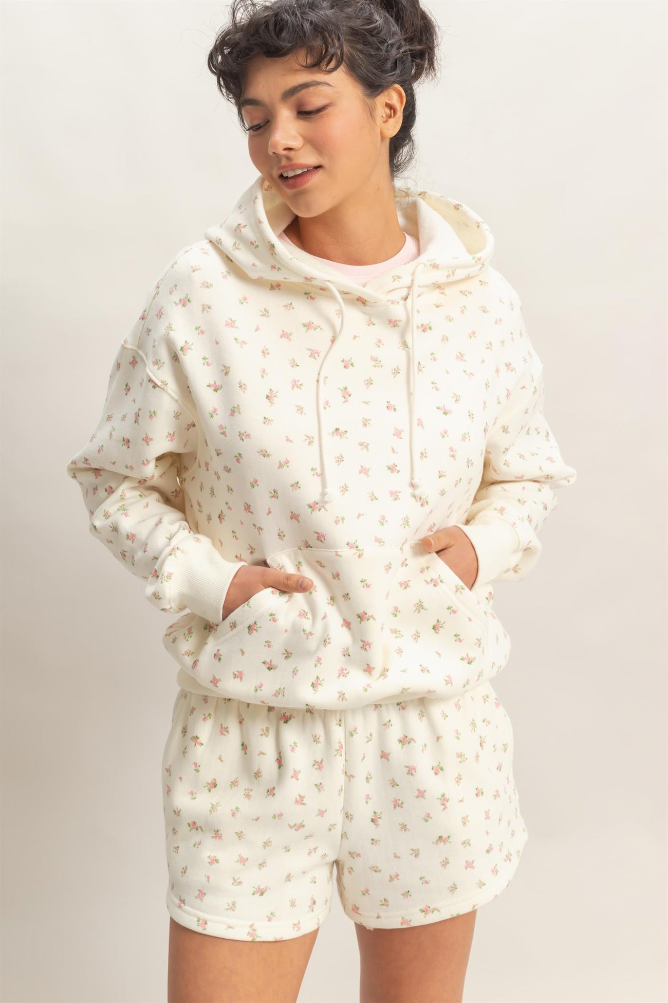 woman wearing a cream hoodie with floral print and matching shorts, hands in pockets, looking relaxed