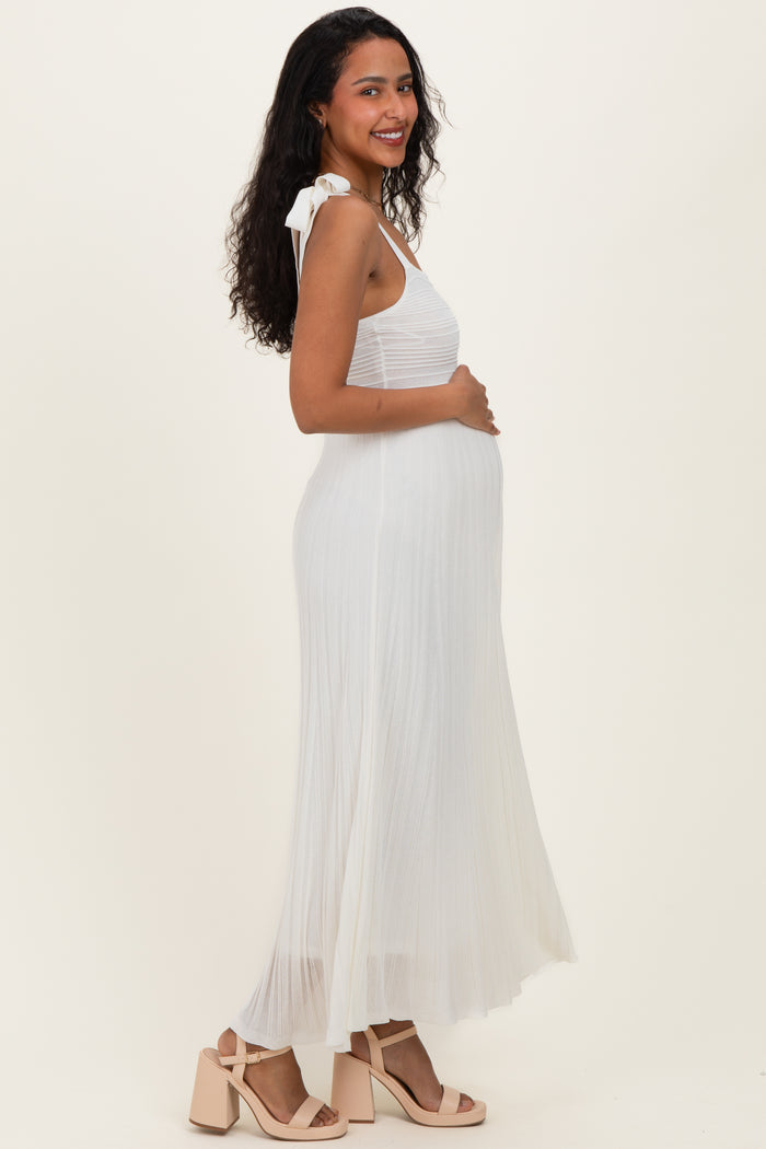 woman wearing a white pleated maternity dress with tie shoulder straps and holding her baby bump