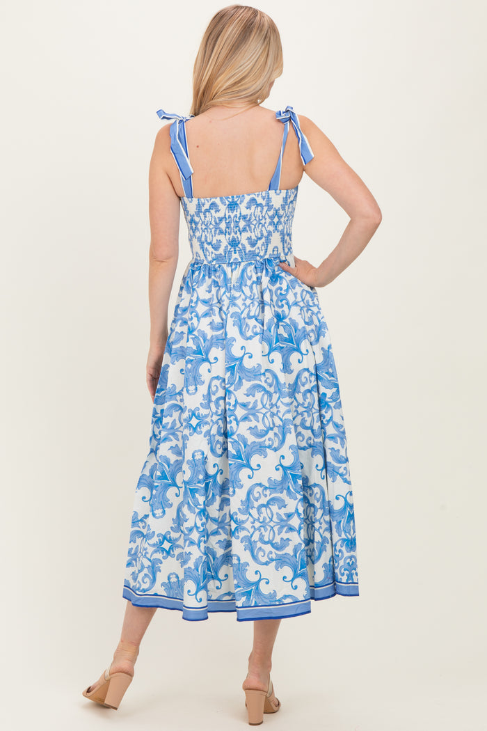 woman wearing a blue and white patterned midi dress with adjustable tie straps and a smocked back