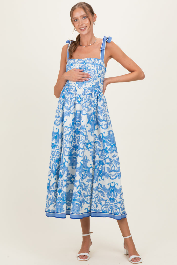 woman wearing a blue and white floral maternity maxi dress with tie straps and holding her baby bump