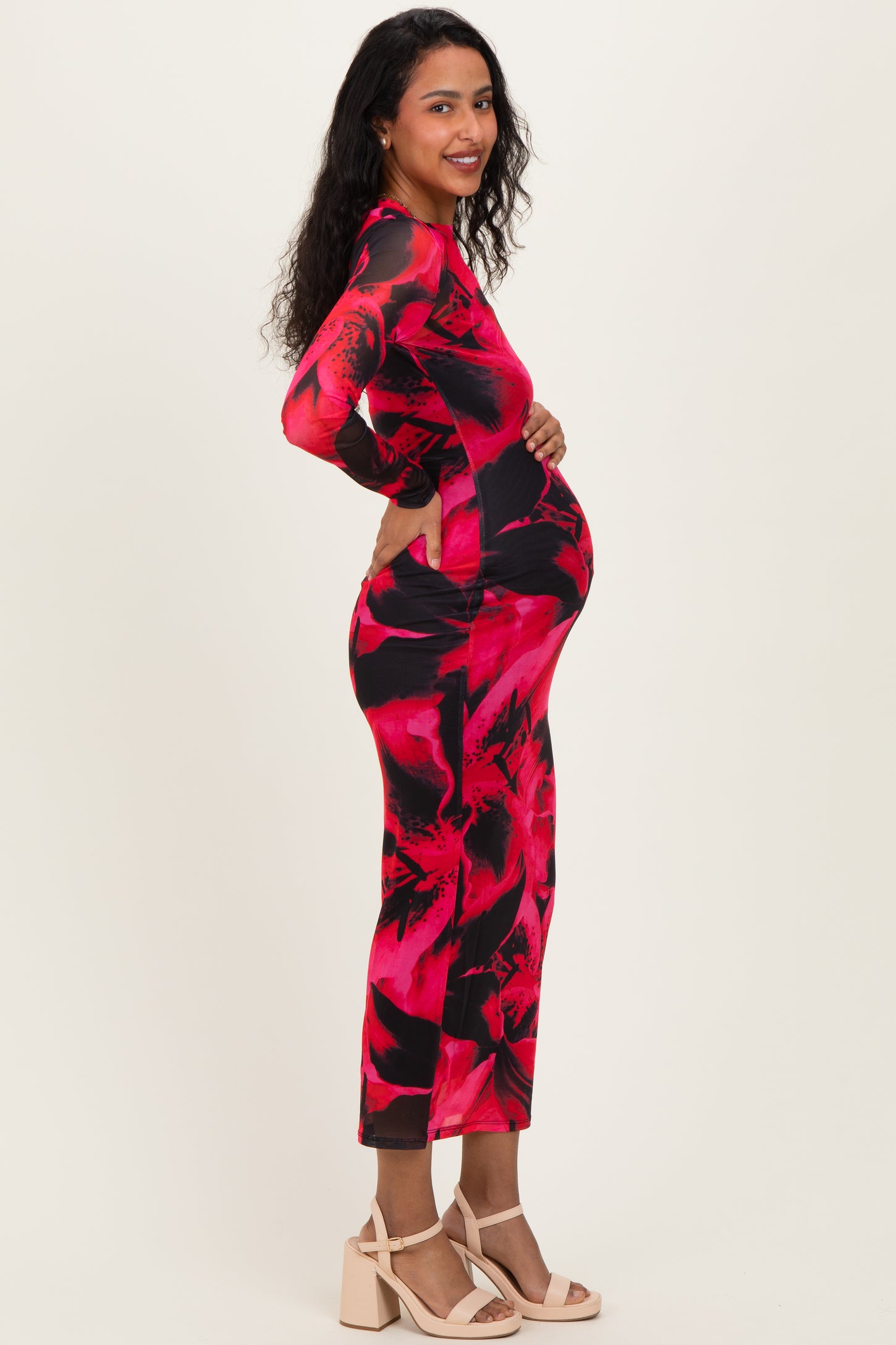 woman wearing a bright red and black floral print maternity dress and displaying her baby bump