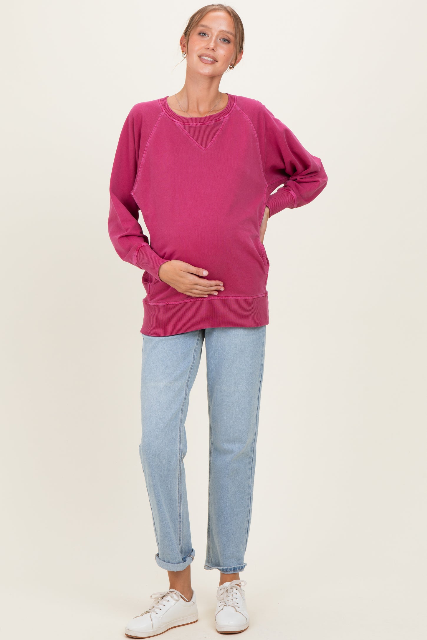 woman wearing a pink oversized maternity sweatshirt and blue jeans, holding her baby bump
