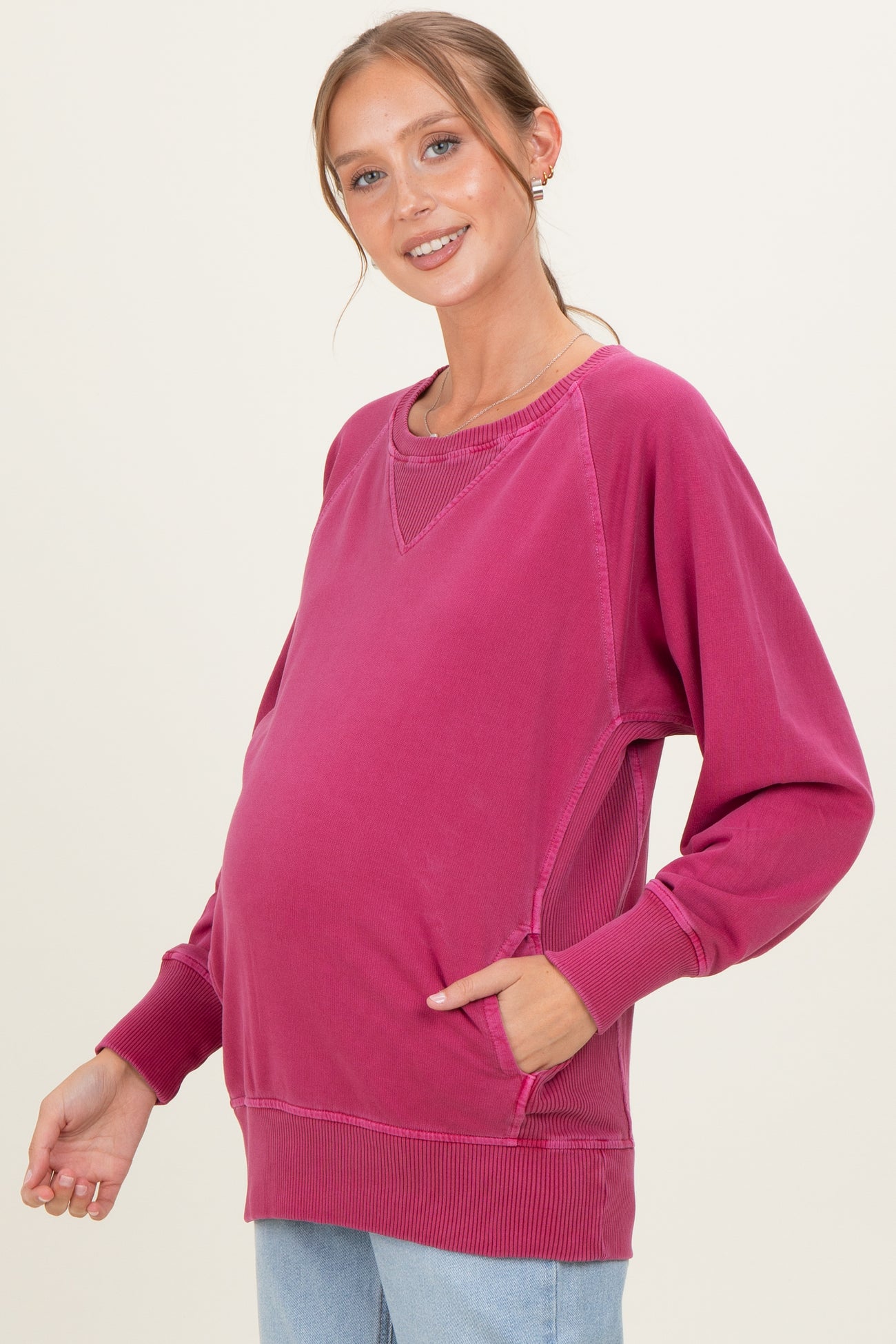 woman wearing a pink maternity sweatshirt with side pockets and a visible baby bump