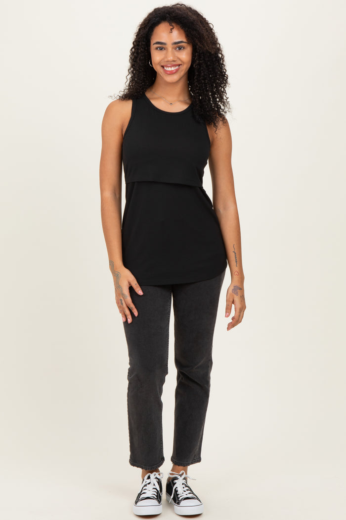woman wearing a black sleeveless top and dark slim-fit jeans with sneakers, smiling at the camera