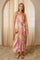 woman wearing a colorful floral maxi dress with a tie waist and spaghetti straps, holding a round clutch bag