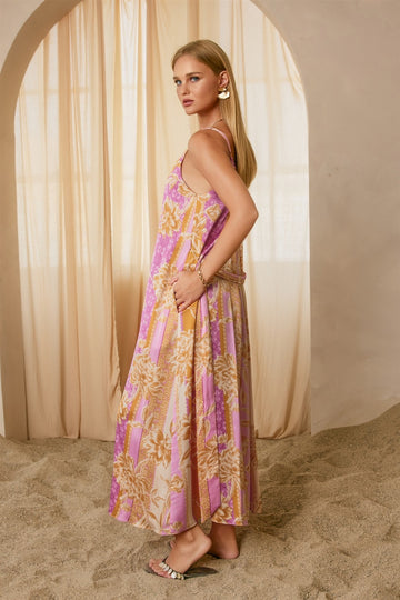 woman wearing a pink and cream floral maxi dress with spaghetti straps, standing against a soft beige backdrop