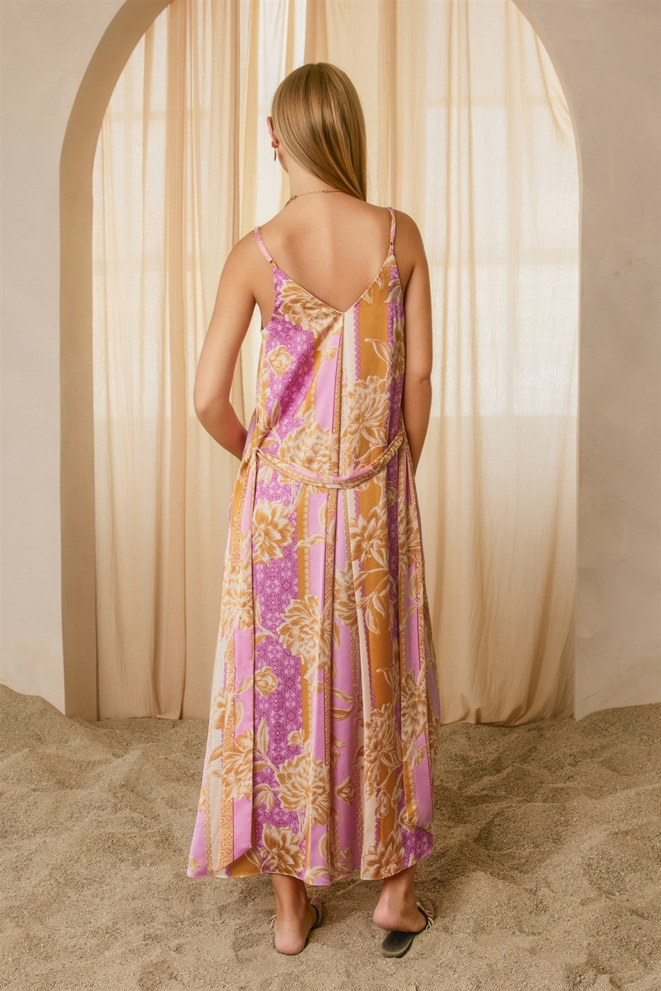 woman wearing a long floral patterned maxi dress with a deep v-back, standing in a sandy setting