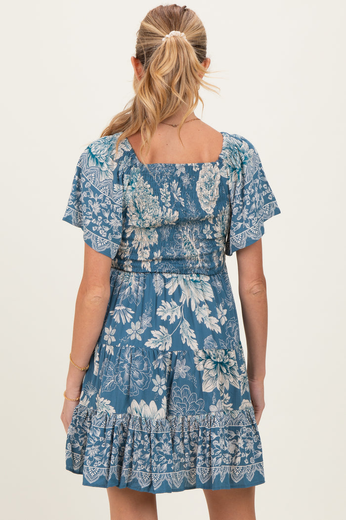 woman wearing a blue floral maternity dress with short flutter sleeves and a ruffled hem, shown from the back