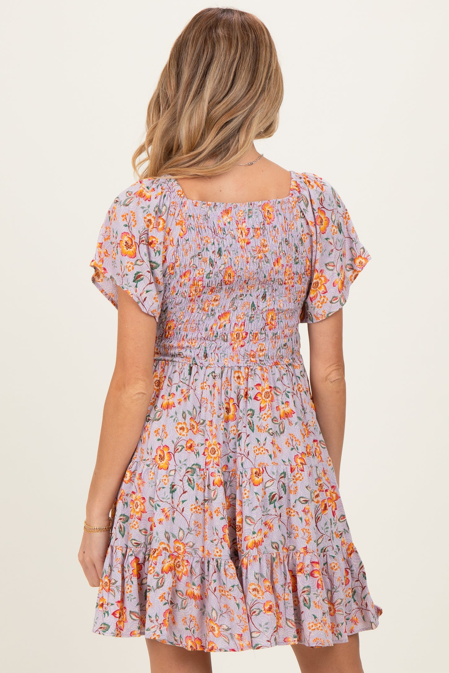 woman wearing a floral smocked maternity dress with flutter sleeves and a ruffled hem, showing the back view