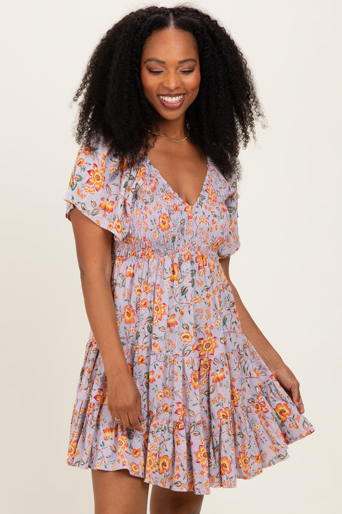 woman wearing a lavender floral short dress with flutter sleeves and a tiered skirt, smiling at the camera