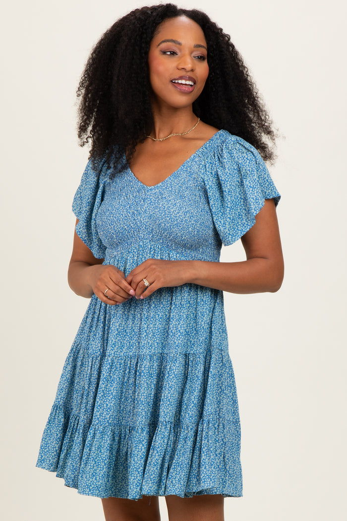 woman wearing a blue floral short sleeve dress with a tiered skirt and a v-neckline