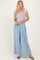 woman wearing a gray short sleeve henley top and light blue wide leg pants standing against a neutral background
