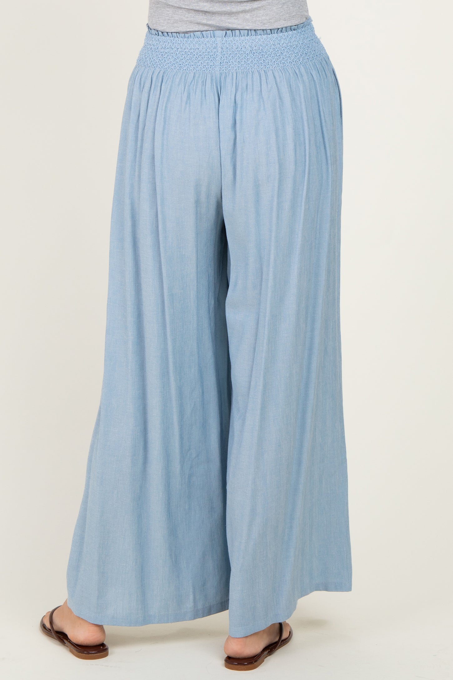 woman wearing light blue wide-leg pants with a smocked waistband, viewed from the back