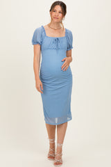 woman wearing a blue polka dot maternity dress with short puff sleeves and a ruched skirt, holding her baby bump