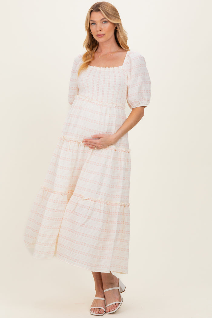 woman wearing a pink and white patterned maternity dress with puff sleeves and tiered skirt, holding her baby bump