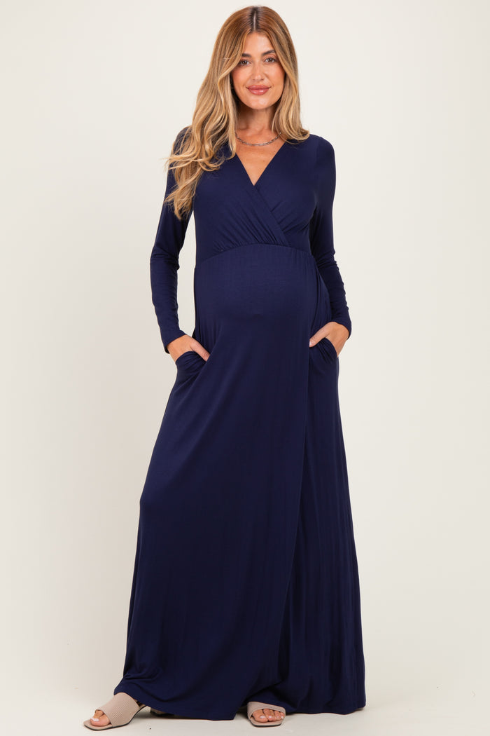woman wearing a navy blue long sleeve maternity maxi dress with a wrap style and pockets, showing her baby bump