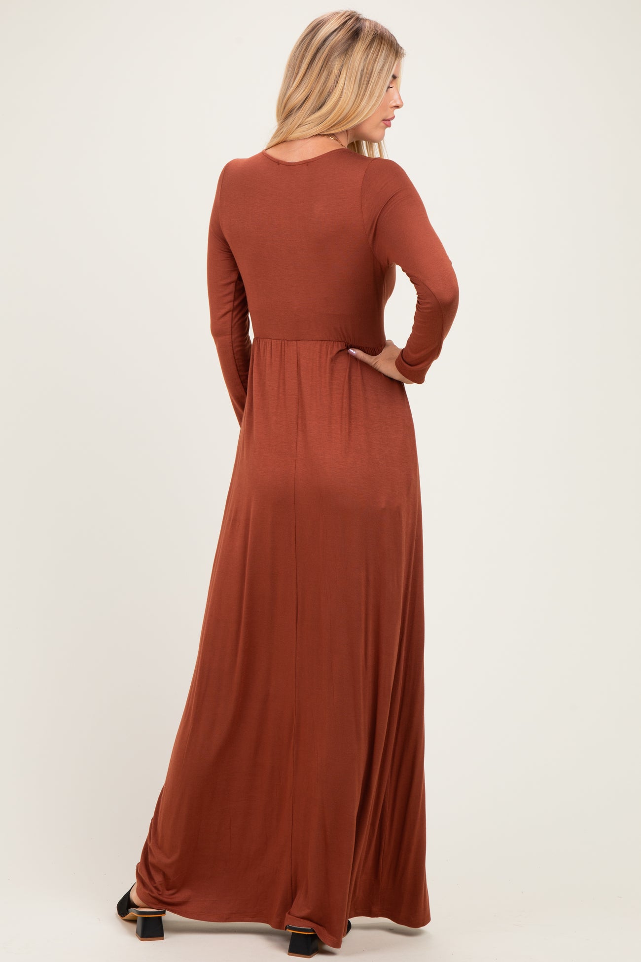 woman wearing a rust long sleeve maxi dress, seen from the back, flowing silhouette, fitted bodice, and flared skirt