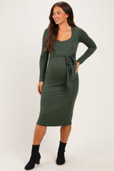 woman wearing a dark green long sleeve maternity dress with a tie waist and showcasing her baby bump