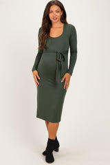 woman wearing a dark green long sleeve maternity dress with a tie at the waist and a visible baby bump