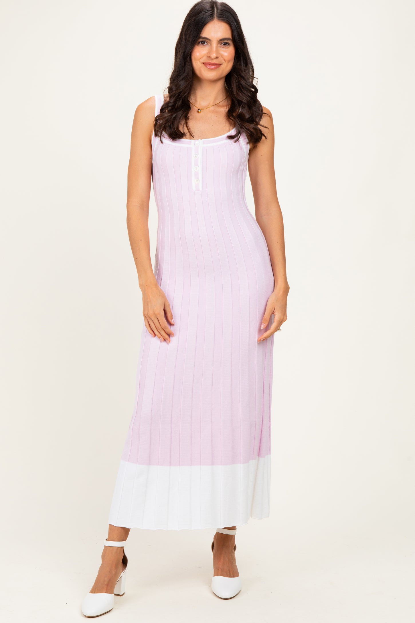 woman wearing a light pink ribbed maxi dress with white hem and decorative buttons, standing with one hand on her hip