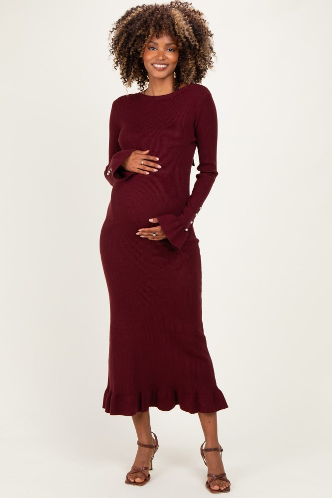 woman wearing a burgundy long sleeve maternity dress with flared cuffs and a ruffled hem, holding her baby bump