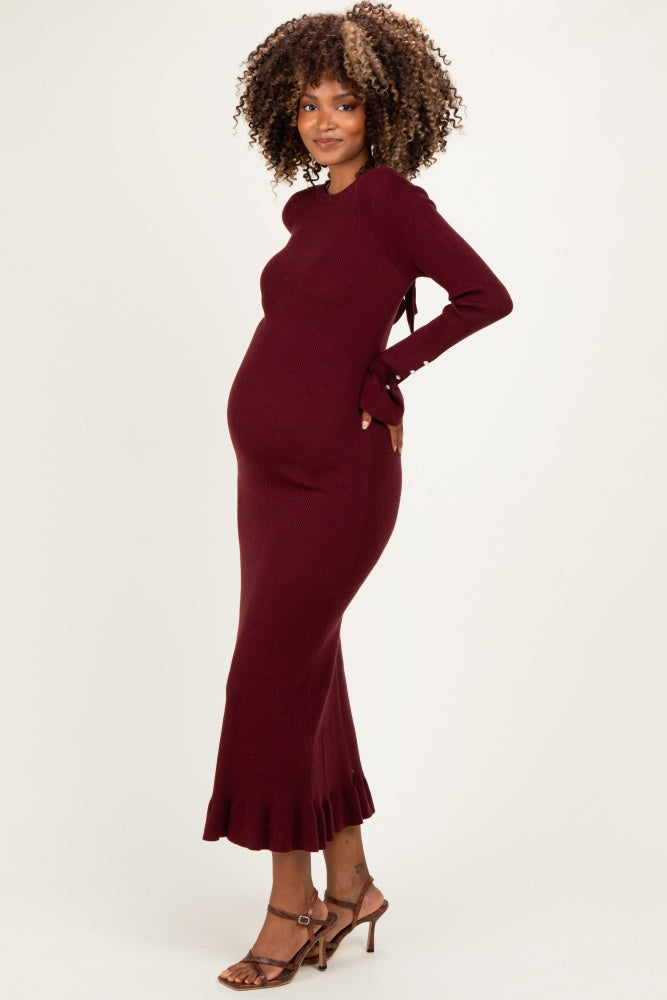 woman wearing a burgundy maternity ribbed knit dress with ruffle hem and holding her baby bump