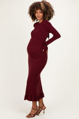 woman wearing a burgundy maternity ribbed knit dress with ruffle hem and holding her baby bump