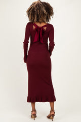 woman wearing a burgundy ribbed maternity dress with a back bow detail and ruffled hem