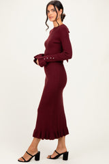 woman wearing a burgundy ribbed midi dress with ruffled hem and button details on sleeves, styled with heeled sandals