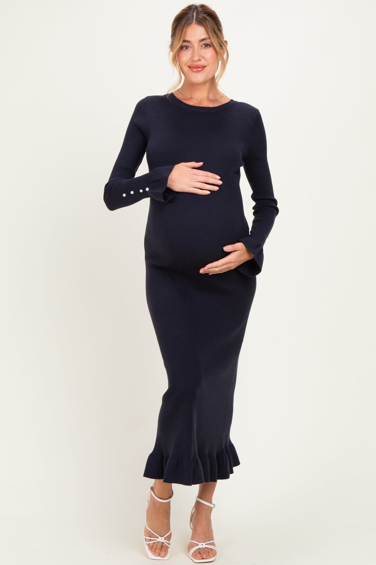 woman wearing a navy blue ribbed maternity dress with bell sleeves and a ruffle hem, holding her baby bump