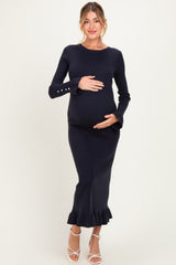 woman wearing a navy blue ribbed maternity dress with bell sleeves and a ruffle hem, holding her baby bump