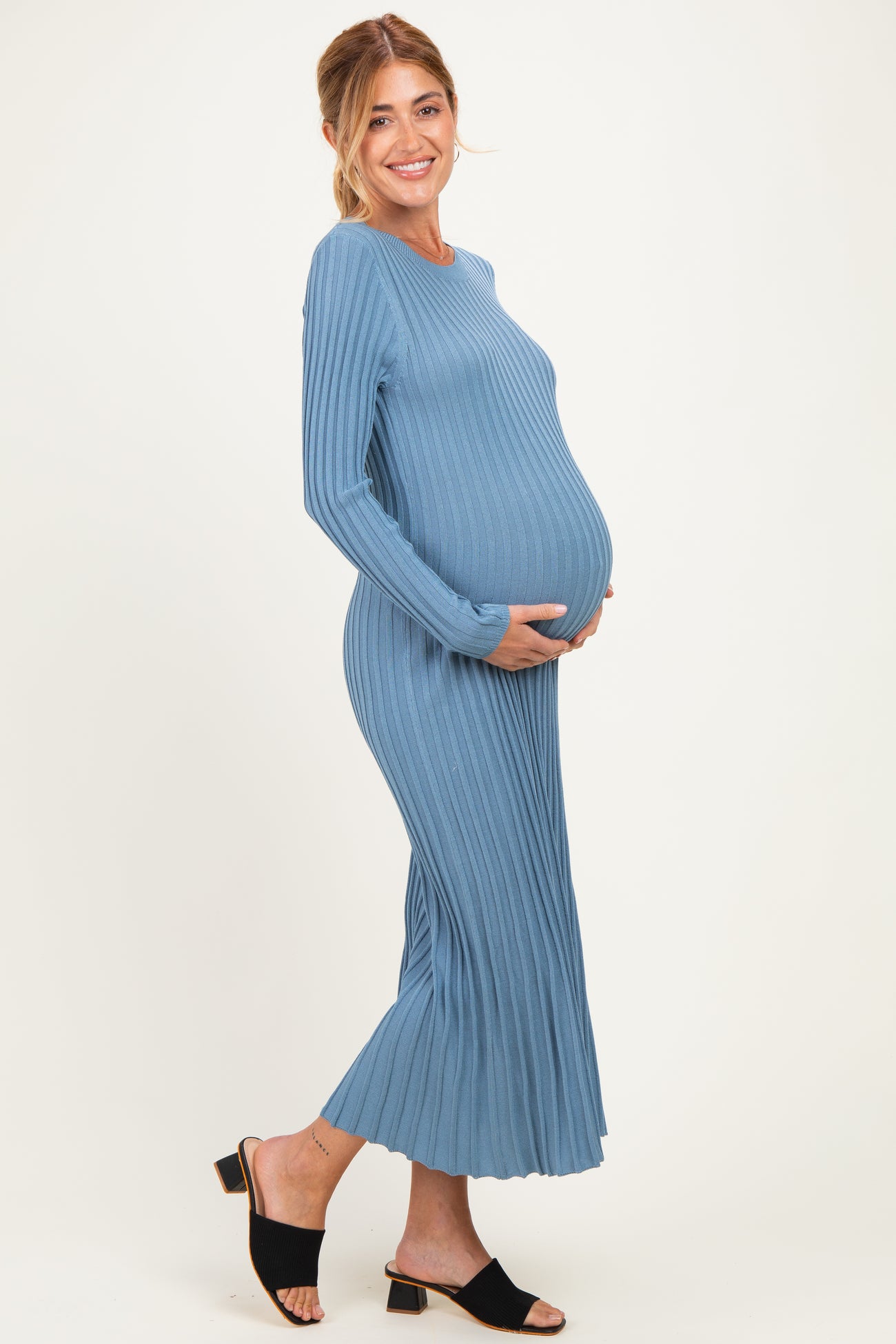 woman wearing a ribbed light blue maternity dress, smiling and showing her baby bump
