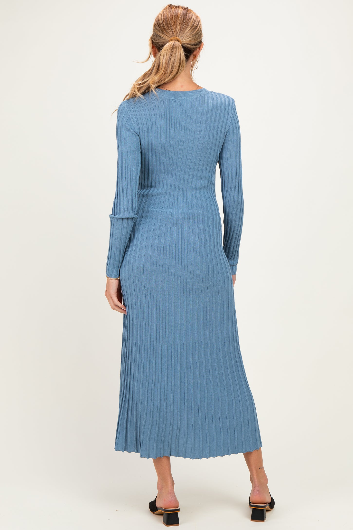 woman wearing a ribbed maternity dress in light blue, long sleeves, and mid-calf length, seen from the back