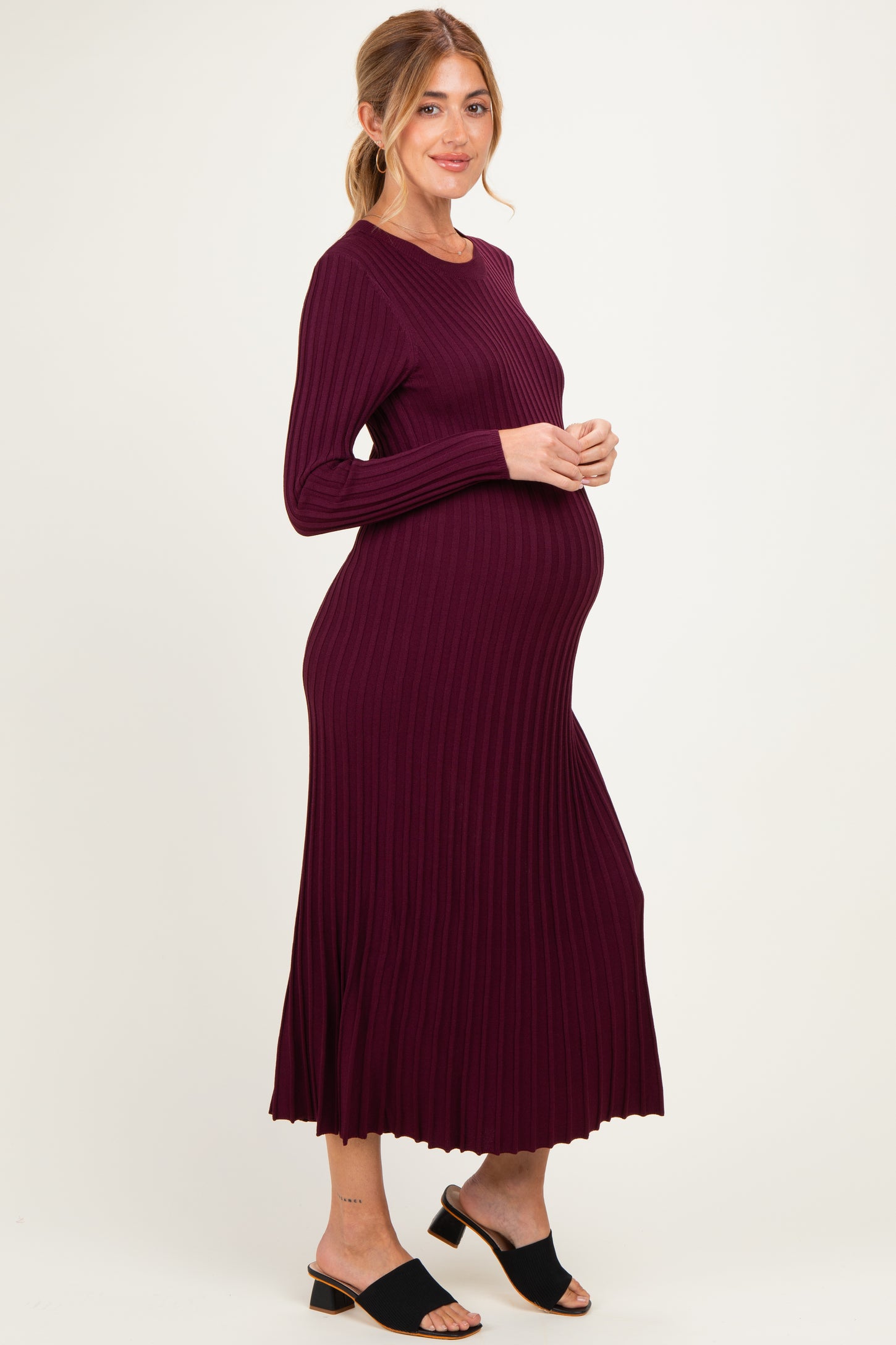 woman wearing a burgundy ribbed maternity dress, showing her baby bump, standing in profile with a relaxed pose